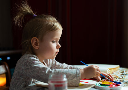 A young baby artist painting with watercolors. Adorable blonde girl of 2,5 years old learns to paint sitting at the table.の写真素材