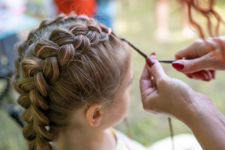 Hairdresser is braiding the hair on a young girl. Braids on the girl's head. Pink thread is woven...