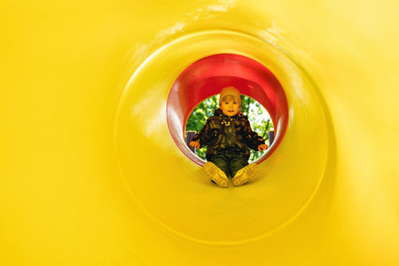 Active little girl inside a tube slide on playground. Cute little girl sliding down on slide....