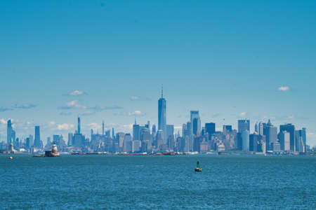 Statue of Liberty and lighthouse in front of Manhattanの写真素材