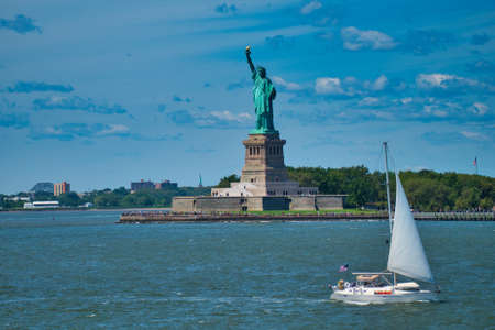 yacht in front of the statue of liberty on a sunny summer dayの写真素材
