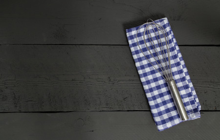 Whisk and tea towel on black wooden background.