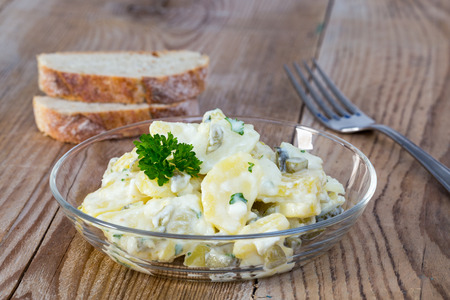 Potato salad in a glass bowl on wooden board.の写真素材