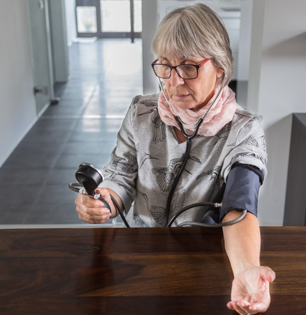 Senior checks blood pressure with measuring instrument on table.の写真素材