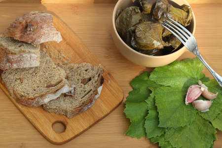 Dolma - grape leaves stuffed with minced meat on a wooden tray with slices of black bread and white garlic sauceの写真素材