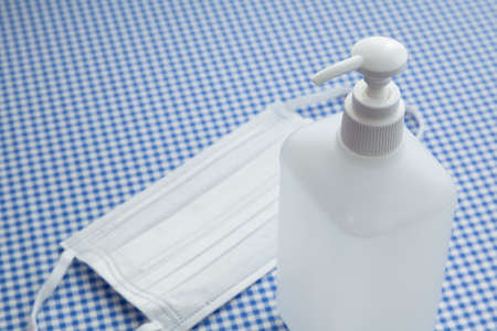 alcohol gel hand sanitizer in pump bottle and face mask on blue and white checkered table clothの写真素材
