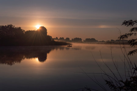 Sunrise on the lake with fog and trees reflected in the waterの写真素材