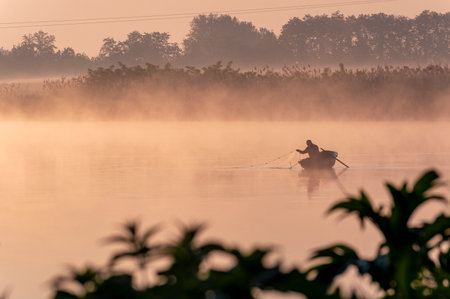 Fisherman in a boat on a foggy lake at sunriseの写真素材