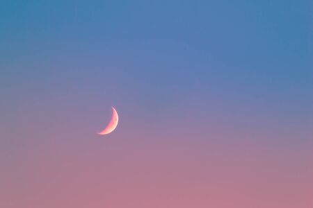 Pink Crescent Moon in blue sky with pink light on Bottom of the pictureの写真素材