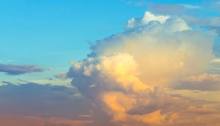 Yellow and orange sunset light in blue sky with soft clouds