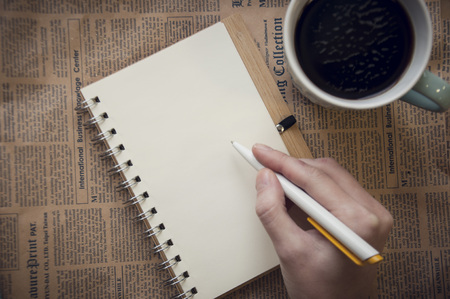 blank notebook with hand holding pen and cofee on brownの写真素材