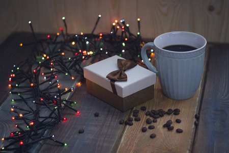 Gift box with bow, blue cup, lights, coffee grains on tableの写真素材