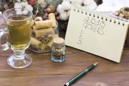 2018 goals inscription in a notebook, a cup of tea, a bowl of cookies and a Christmas wreath