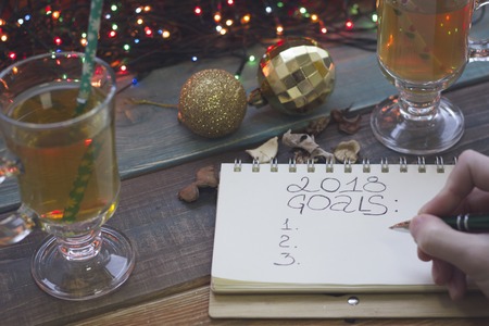A hand writing 2018 goals in a notebook, two tea cups, Christmas-tree toysの写真素材