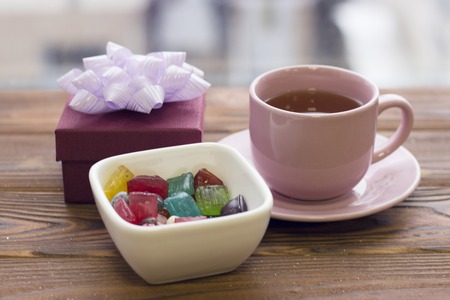 A tea cup with a saucer, a gift box and a bowl of colored candiesの写真素材