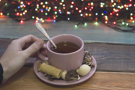 A hand holding a cup of tea with a teaspoon and a saucer, fairy lightsの写真素材