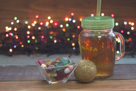 A festive still life with a glass clear cup of tea with a cap, a bowl of candies,a golden ball, fairy lightsの写真素材