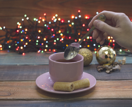 A hand holding a teaspoon, a cup of tea with saucer, Christmas-tree toysの写真素材