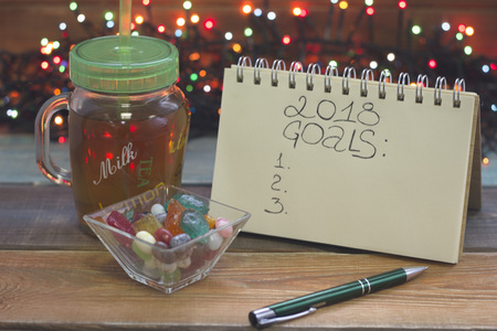 A festive still life with a glass clear cup of tea with a cap, 2018 goals inscription, a bowl of candies, fairy lightsの写真素材