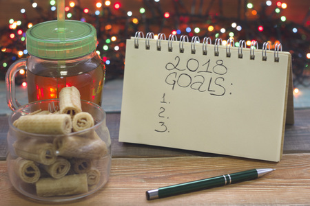 A festive still life with a glass clear cup of tea with a cap, 2018 goals inscription, a bowl of...