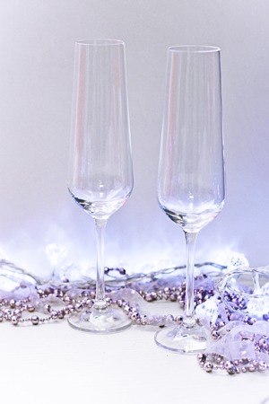 Two clear empty champagne glasses with a Christmas garland of beads and ribbon and white fairy lights. Light background.の写真素材