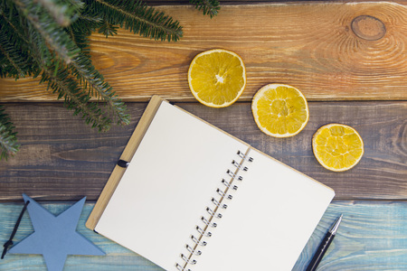 A colored wooden Christmas or New Year background with fir tree branches, a blank notebook and and slices of a fresh orange.の写真素材