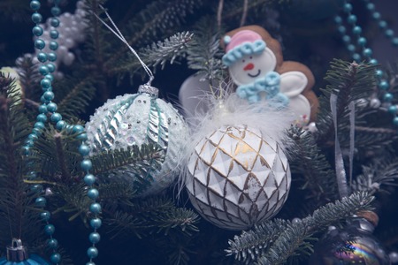 Unusual white Christmas-tree balls with glitter, blue and white beads and a gingerbread cookies on fir tree branches. Close up. Christmas or New Year banner.の写真素材