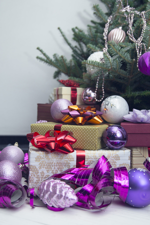 New Year's decor idea for a living room with gifts under a Christmas tree. A pile of gift boxes with bright ribbons and shiny purple Christmas-tree ornaments. Light backgroundの写真素材