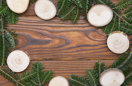 Wooden Christmas or New Year background with a frame made of natural fir tree branches and wooden slices on a rustic wooden table. Space for your text or image.Top view.の写真素材
