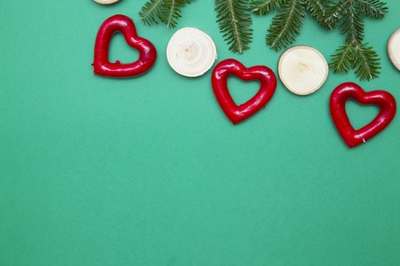 New Year composition with tree red hearts, round pices of wood and natural spruce branch. Green one-color Christmas or New Year background. Space for your text or image. Top view.の写真素材