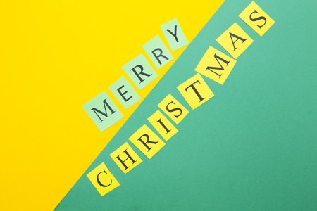 Merry Christmas diagonal inscription on a green and yellow paper background. Space for your text or image. Top view.の写真素材