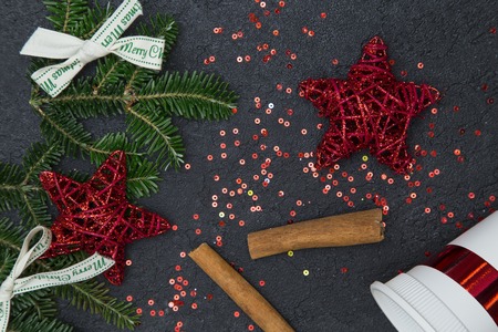 Cinnamon sticks, white bows, white paper cup, red stars and red sequins spread on a black concrete surface. Christmas or New Year background. Top view.の写真素材
