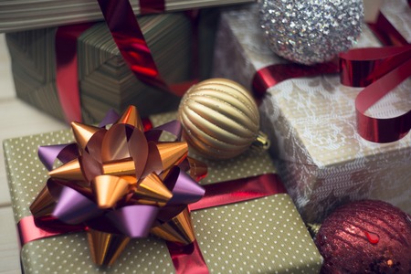 A golden gift box with red metallic ribbon and and orange-purple in a close up with other gift boxes...