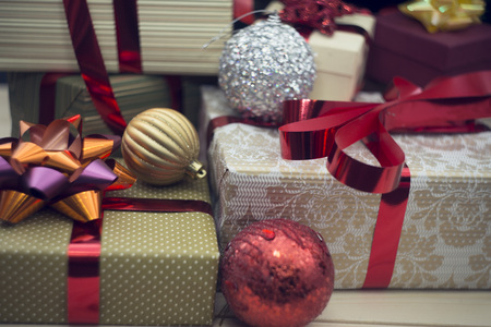A golden gift box with red metallic ribbon and and orange-purple in a close up with other gift boxes glitter Christmas-tree ballsin silver, gold and red colors.. Close up. Christmas or New Year banner.の写真素材