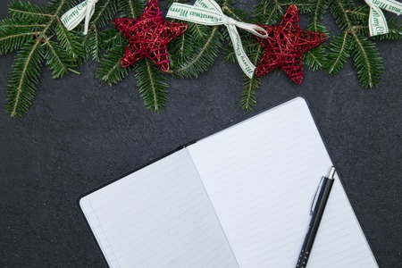 A blank notebook with spruce branches, white bows and red stars on a black concrete surface. Christmas or New Year background. Space for your text or product display. Top view.の写真素材