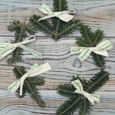 A wreath of spruce branches and white textile bows with Merry christmas inscription. Light wooden shabby background for Christmas or New Year. Space for your text or product display. Top view.の写真素材