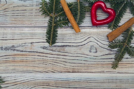 Light wooden shabby background for Christmas or New Year with a corner frame of spruce branches,cinnamon sticks and a red heart. Space for your text or product display. Top view. Close upの写真素材