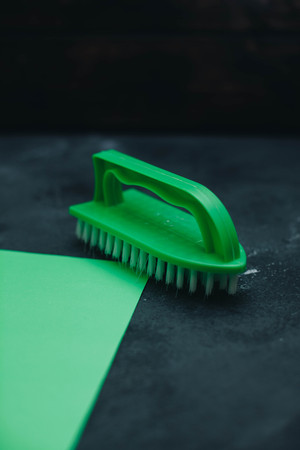 Green plastic clothes brush and cleaning rag on a black concrete background. Composition for...