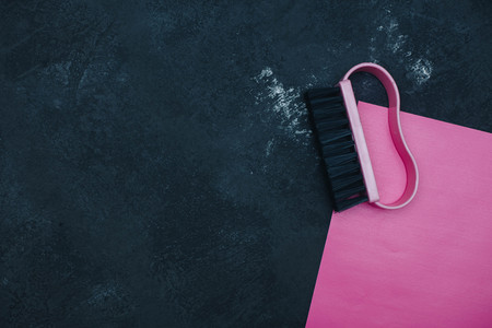 A bright composition with a pink clothes brush on pink paper. Black concrete background. Top view