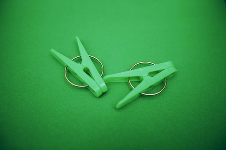 Green plastic clothes clothes pegs on a bright one-color green background. Top view. Household...