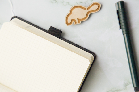 Collect your creative ideas in an opened blank notebook. A black pen and a wooden pin on a white marble table. Space for your text or produst display.の写真素材