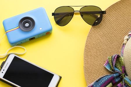Photo camera, black aviator sunglasses mobile phone and a straw hat on a bright yellow background. Travel mock up, top view.の写真素材