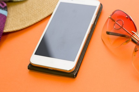 Planning a trip. Mobile phone and sunglassess on a bright orange background, close up.の写真素材