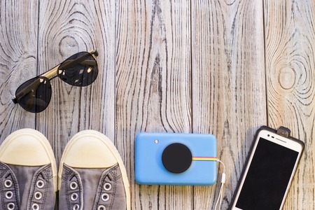 Traveller's hipster outfit- sport shoes, sunglasses, photo camera and mobile phone on a wooden background. Spase for your text or image.の写真素材