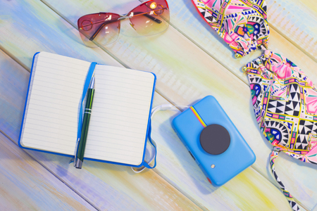Travelling inspiration. Write your creative ideas. Tourist's accessories on a colored wooden table- a swim suit, a notebook, a camera and sunglasses. Tourism concept background, top view.の写真素材