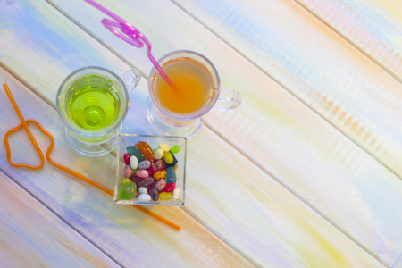 Relaxing on a vacation with tropical cocktails and a bowl of candies on a light colored wooden table. Space for a text or product display, top view.の写真素材