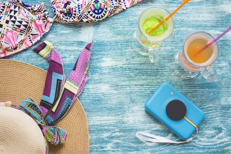 Couple enjoy seaside vacation- tropical cocktails, a swimsuit, a straw hat and camera on a blue wooden background. Space for a text or product display, top view.の写真素材