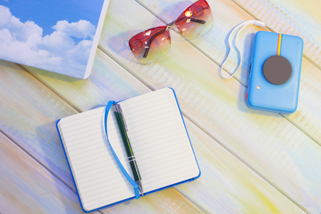 Travelling inspiration. Write your creative ideas. Tourist's items on a colored wooden table- notebooks, a camera and sunglasses. Tourism concept background, top view.の写真素材