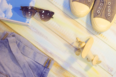 Vacation items on a light colored wooden table- denim shorts, sport shoes, a toy airplane,a notebook and sunglasses. Tourism concept background, top view.の写真素材
