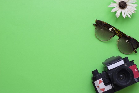 Green tourism concept background with flower, camera and sunglasses, top view. Space for a text or product display.の写真素材